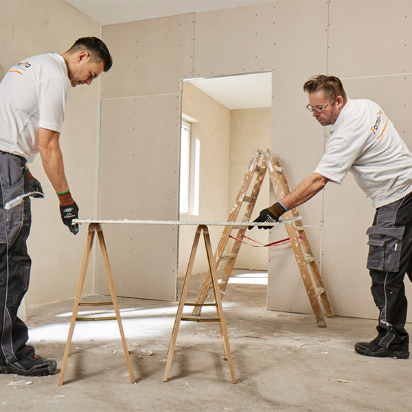 Zwei Männer in einem Raum arbeiten an einer Dämmung auf zwei Holzböcken