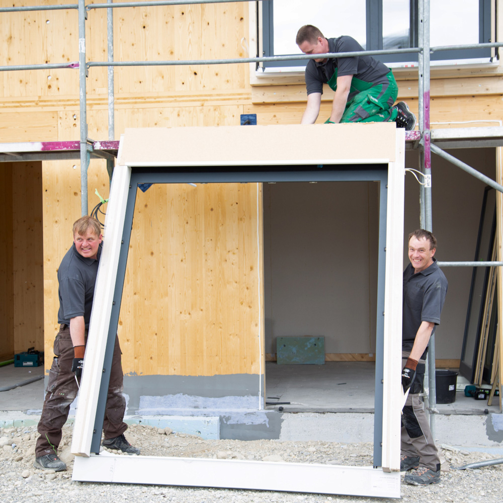Drei Männer an einer Baustelle halten einen Fensterrahmen